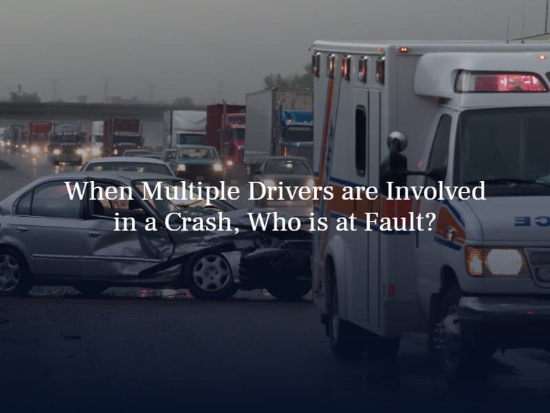 ambulance parked in front of a smashed sedan on a busy road with cars and trucks coming. text: "When multiple drivers are involved in a crash, who is at fault?"